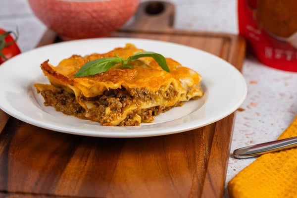 A slice of Rogan Josh lasagne with spiced lamb mince, white sauce and golden melted Cheddar, served with a side salad